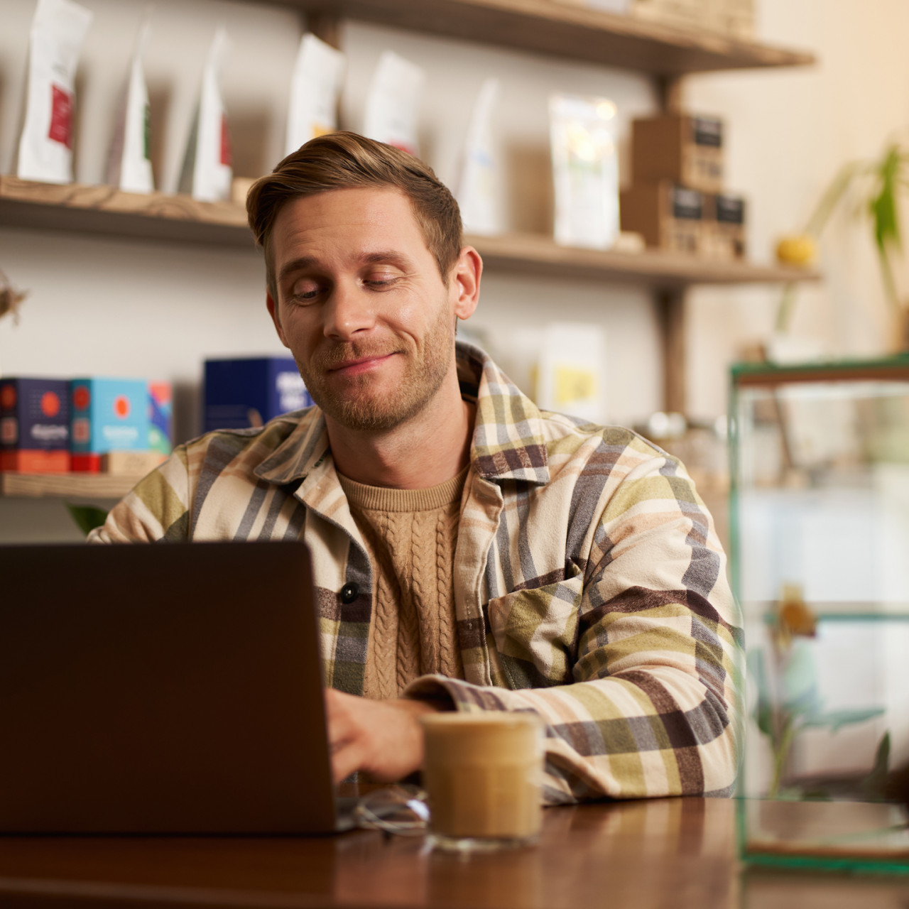 Photo of a smiling man working on his laptop at a coffee shop.